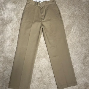Dickies - Snygga beige byxor från Dickies med klassisk design. De har en rak passform och är tillverkade i ett slitstarkt material. Perfekta för en stilren look. Byxorna har hällor för bälte och en diskret logga baktill.