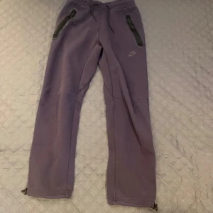 Mörkblå mjukisbyxor Nike -  Ett par bekväma mjukisbyxor från Nike med snörning i midjan och dragkedjor vid fickorna. Byxorna har en mer straight passform och är väldigt bekväma. 