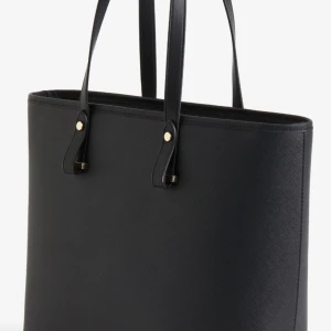 Svart shoppingväska med gulddetaljer - Stilren svart shoppingväska med eleganta gulddetaljer på handtagen. Perfekt för att bära med sig allt man behöver under dagen. Väskan har en enkel och tidlös design som passar till många olika stilar.