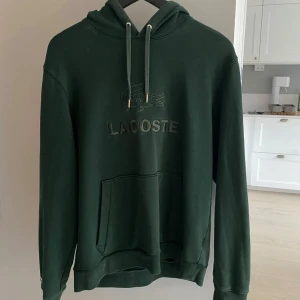 Mörkgrön hoodie från Lacoste - Säljer en snygg mörkgrön hoodie i märket Lacoste med broderad logga på bröstet. Tröjan är köpt på NK i Göteborg för nypris 1499! Den är fortfarande i ett mycket bra skick och säljs nu för endast 799kr! Skriv vid frågor! 