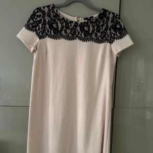 Kort klänning med spets  - En kort beige-rosa klänning från H&M som knappt är använd. Den är rak i modellen och kort. Över axlarna är det en fin spets.