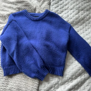 Blå stickad tröja - Säljer en mysig blå stickad tröja med rund hals och långa ärmar. Perfekt för kyligare dagar och ger en avslappnad look. Tröjan har ribbade muddar vid ärmslut och nederkant.