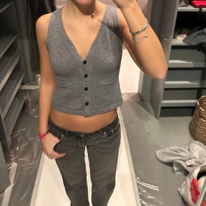 Grå ribbad väst - Snygg grå ribbad väst med knappar framtill. Västen är ärmlös och har en v-ringad design som ger en stilren look. Perfekt för att lägga till en extra touch till din outfit.