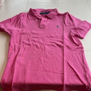 Rosa pikétröja från Ralph Lauren - Säljer en snygg rosa pikétröja från Ralph Lauren i slim fit. Tröjan har en klassisk krage och korta ärmar med det ikoniska gröna broderade logotypen på bröstet. Perfekt för en stilren look!