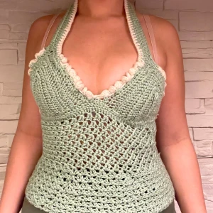 Grön virkad halterneck-top - Säljer en superfin grön virkad halterneck-top med vita detaljer. Toppen är perfekt för sommaren och har en snygg öppen design som ger en luftig känsla. Den är handgjord av mig och passar perfekt till både stranden och sommarfester!