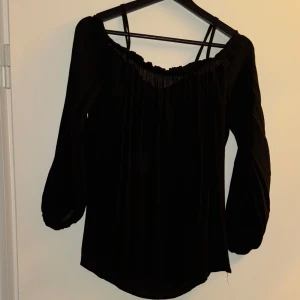 Svart offshoulder topp från Zara - Säljer en elegant svart offshoulder topp från Zara. Den har långa ärmar och en smickrande passform som passar perfekt för både vardag och fest. Toppen är i storlek XS och är tillverkad i ett mjukt och bekvämt material.