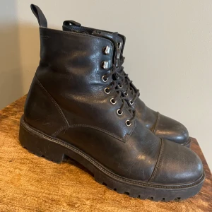 Svarta kängor i skinn - Ett par robusta svarta kängor i skinn fr Vagabond. Grov sula med snörning framtill, vilket ger dem en tuff look. Perfekta för höst och vinter, i använt skick men fortfarande i bra form. Behöver putsas upp, annars perfekt. Finns i butik för 1400.