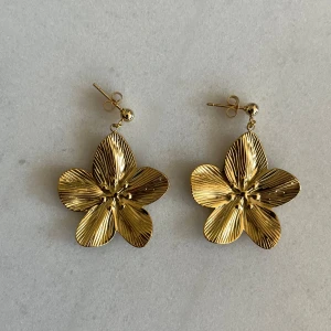 Guldiga blomformade örhängen - Säljer ett par superfina guldiga örhängen i form av blommor. De har en vacker, glansig yta och är perfekta för att ge en extra touch till din outfit. Passar perfekt till både vardag och fest!