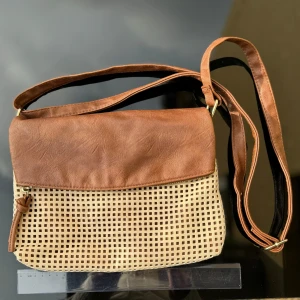 Don Donna Brun och beige axelväska   - Axelväska från Don Donna i brunt och beige. Väskan har en cool flätad design på framsidan och en praktisk dragkedja på baksidan. Justerbar axelrem och flera fack inuti. Mått -se linjal på bild. Hämtas på Hägerstensåsen eller ök 🤎