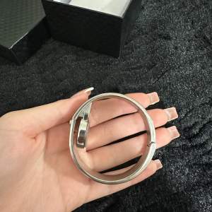 Säljer en elegant armbandsklocka i silverfärg. Klockan har en stilren design med en oval urtavla och romerska siffror. Armbandet är stelt och dekorerat med glittriga stenar, vilket ger en lyxig känsla. Perfekt accessoar för både vardag och fest!