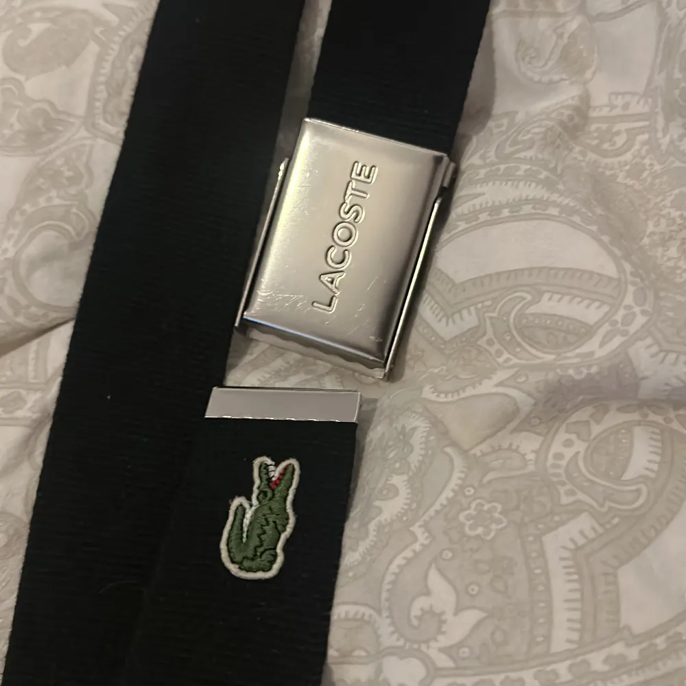 Svart Lacoste bälte med silverspänne. 97 cm.. Accessoarer.