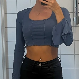 Blå ribbad croppad topp - Säljer en superfin blå ribbad topp med långa ärmar och volangdetaljer vid ärmsluten. Toppen är croppad och har en snygg öppen rygg med knytband. Perfekt för en somrig dag eller en utekväll!