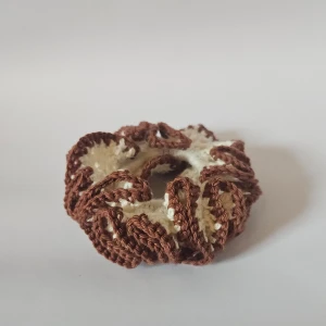 Brun och vit virkad scrunchie - Superfin scrunchie i brunt och vitt, perfekt för att piffa upp vilken frisyr som helst. Den är virkad och har en härlig textur som ger en unik look. Passar både till vardags och fest!