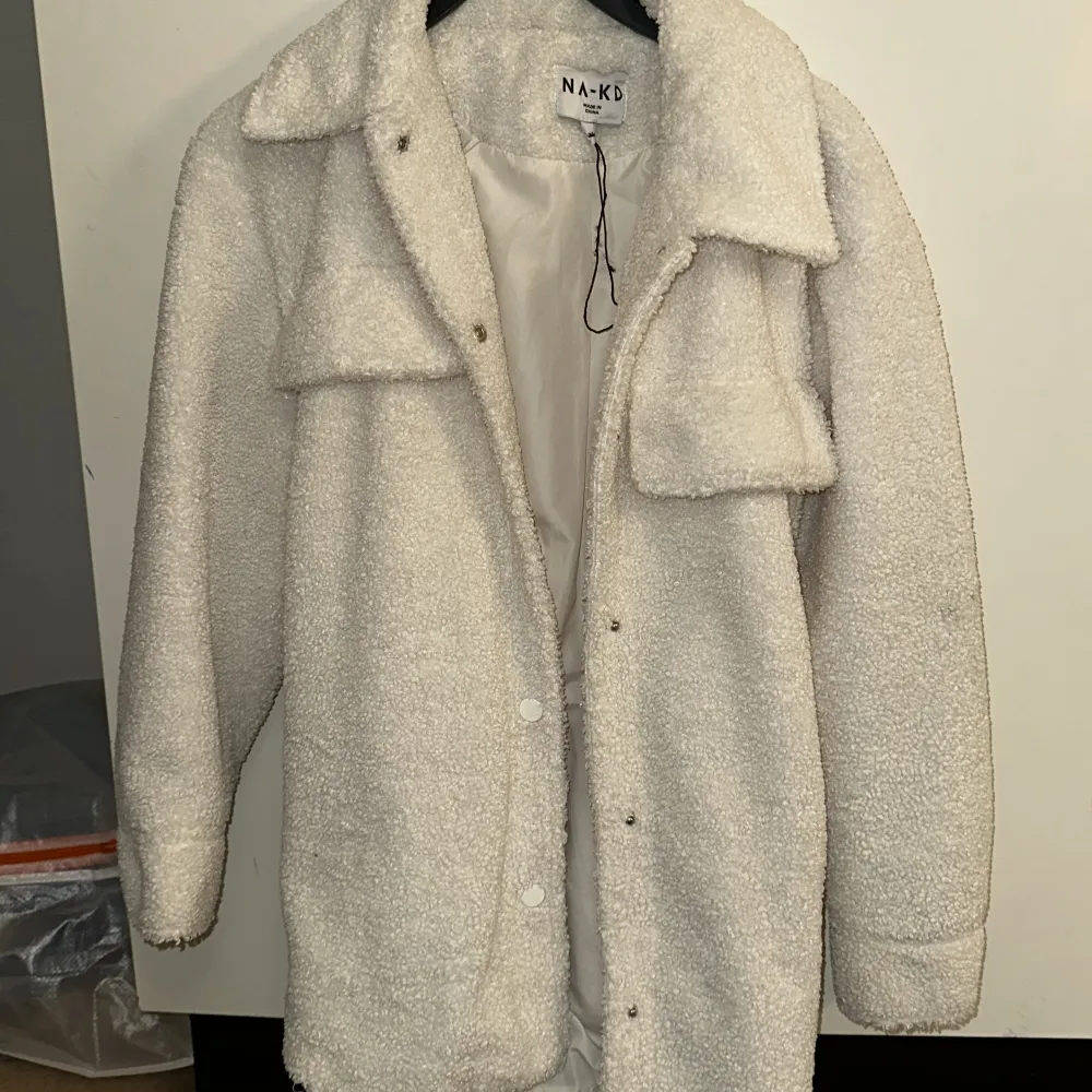 Säljer en supermysig vit teddyjacka från NA-KD. Den har en skön oversized passform och är perfekt för höst och vinter. Jackan har långa ärmar och stängs med knappar framtill. Den har också ett bälte i midjan för en snygg siluett. Två stora fickor framtill ger en cool look. Perfekt för att hålla sig varm och stilren!. Takit.