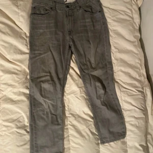 Grå jeans från Dressmann - Säljer ett par grå jeans från Dressmann i 100% bomull. De har en klassisk femficksdesign med knapp och dragkedja framtill. Perfekta för en avslappnad stil.