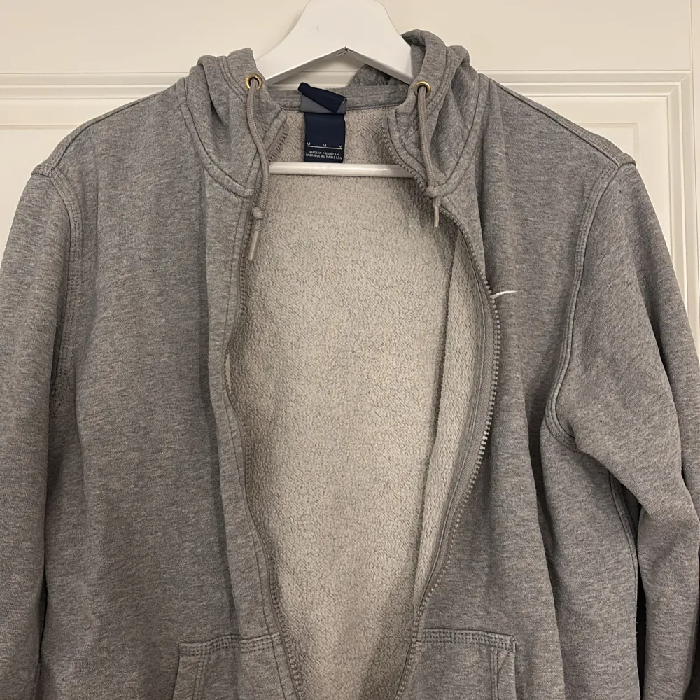 Säljer en grå hoodie med dragkedja och huva. Tröjan har långa ärmar och en liten Nike-logga på bröstet. Perfekt för en avslappnad stil. Lite urtvättad men fortfarande skön. Stl M, 65cm lång. Hupparit & Collegepaidat.