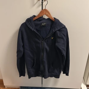 Mörkblå hoodie från Lyle & Scott - Säljer en mörkblå hoodie från Lyle & Scott med dragkedja och huva. Perfekt för en avslappnad stil. Den har en liten logga på bröstet och är i en bekväm passform.