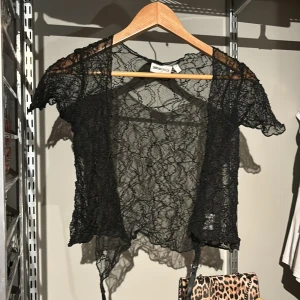Svart spetsbolero från Gina Tricot.  - Säljer en elegant svart spetsbolero från Gina Tricot. Den har korta ärmar och knytband framtill. Perfekt för att lägga till en touch av stil till din outfit.