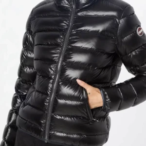 Svart glansig dunjacka - Snygg svart glansig dunjacka från Colmar med dragkedja och hög krage. Perfekt för kyliga dagar med sin design och bekväma passform. Jackan har långa ärmar och en logga på ärmen. Pris kan diskuteras vid snabb affär!!!! 