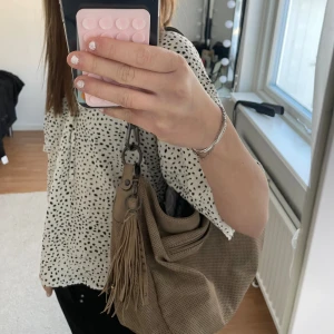Beige axelväska med fransar - Snygg beige axelväska från Suri Frey med fransar som man kan spänna loss. Bra skick förutom en defekt på ena sidan, själva ”draget”  till en dragkedja har gått av. Därav priset, köpt för 750. 💞💞