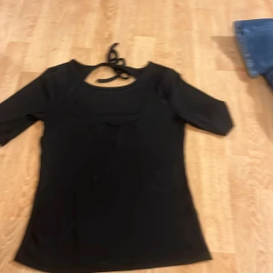 Svart ribbad topp med knytband - Snygg svart ribbad topp med trekvartsärm och knytband i nacken. Perfekt för en stilren look.