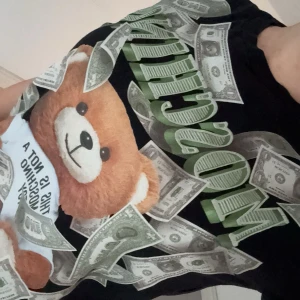 Svart t-shirt med nalletryck från Moschino - Cool svart t-shirt från Moschino med ett stort tryck av en nalle och sedlar. T-shirten har korta ärmar och en normal passform. Knappast använd, inköpt på farfetch.