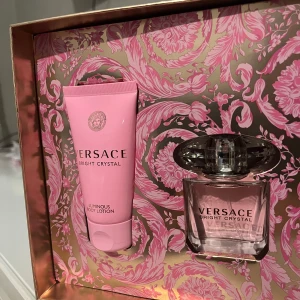 Versace Bright Crystal presentset - Elegant presentset från Versace med Bright Crystal parfym och matchande body lotion. Parfymen kommer i en stilren flaska med en kristalliknande kork, medan body lotionen är i en rosa tub. Förpackningen har ett lyxigt mönster i rosa och guld.