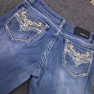 Blå jeans med broderade detaljer från Grace - Snygga blå jeans från Grace med unika broderade detaljer på bakfickorna. Jeansen har en klassisk femficksdesign och en bekväm passform. Perfekta för dig som vill ha något extra i garderoben.