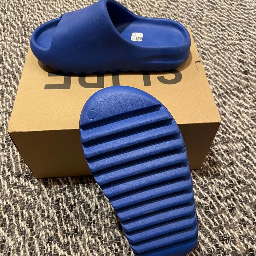 Säljer ett par blå YZY Slide från Adidas. Dessa sandaler har en stilren design med en bred rem över foten och en räfflad sula för extra grepp. Perfekta för en avslappnad stil.. Kengät.