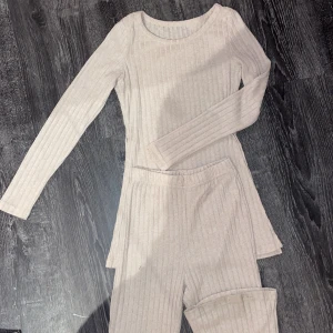 Beige ribbad klänning och byxor från Shein - Säljer ett set med en beige ribbad klänning och matchande byxor från Shein. Klänningen har långa ärmar och en enkel design som passar perfekt för en stilren look. Byxorna är i samma ribbade material och har en bekväm passform.