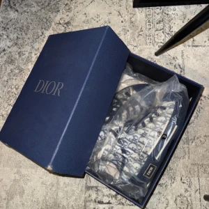 Dior B23 high top  - Snygga Dior sneakers med det ikoniska monogrammönstret i blått och vitt. Skorna har en hög modell med snörning och en robust sula. Perfekta för att ge din outfit en lyxig touch. En skotvätt och de är som nya!