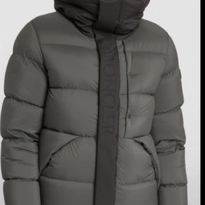 Grå dunjacka från Moncler Mandera  - Anvädts endast 1 gång. Snygg och varm grå dunjacka från Moncler med hög krage och knappar. Perfekt för kyliga dagar. Passar vikt 80 kg +, Längd 175 cm + 