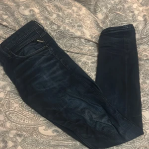 Mörkblå jeans från Replay - Snygga mörkblå jeans från Replay i modell Anbass. De har en klassisk femficksdesign och en knappgylf. Perfekta för en stilren look.