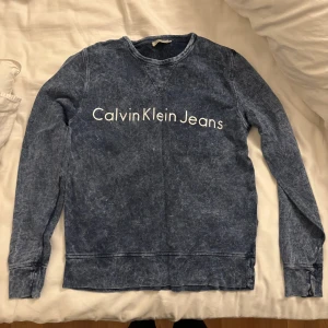 Blå tröja från Calvin Klein Jeans - Säljer en snygg blå tröja från Calvin Klein Jeans med tryck framtill. Tröjan har långa ärmar och en avslappnad passform, perfekt för en casual look. Den är tillverkad i ett mjukt material som känns skönt mot huden.