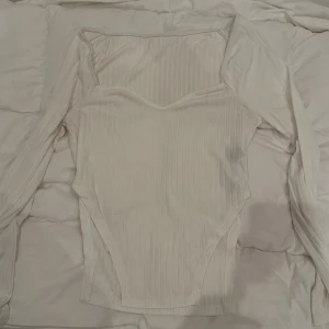 Vit ribbad topp från SHEIN - Säljer en stilren vit ribbad topp från SHEIN. Toppen har en elegant offshoulder-design och är tillverkad i ett mjukt och stretchigt material. Perfekt för att skapa en chic look.