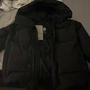 Canada goose jacka macmillian - Säljer en svart dunjacka från Canada Goose med huva och dragkedja. Jackan har en broderad logotyp på ärmen och är perfekt för kalla dagar. Den är både stilren och funktionell. Det är storlek S, den är helt ny.