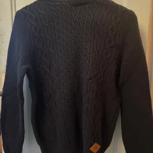 Mörkblå stickad hoodie - Säljer en mörkblå stickad hoodie med kabelstickat mönster framtill. Aldrig använt så mycket fint skick i storlek 170.