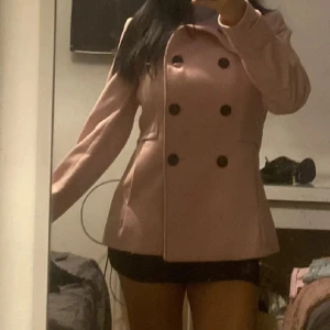  kappa  - Snygg rosa kappa från H&M med dubbelknäppning och hög krage. Perfekt för kyligare dagar med sin stilrena design och långa ärmar. Ett måste i garderoben för en chic look.