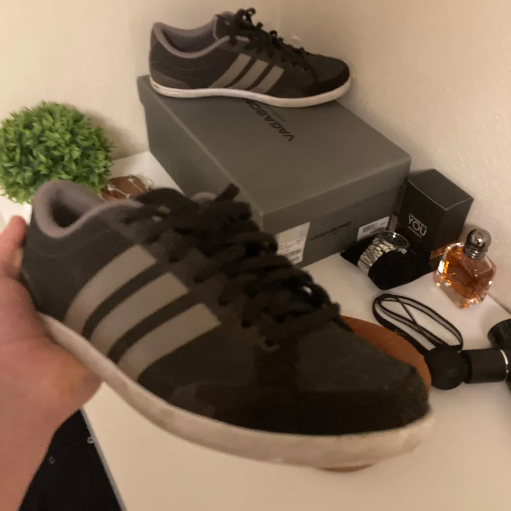 Säljer ett par snygga svarta Adidas sneakers i storlek herr 41,5. De har de klassiska tre ränderna i grått på sidan och är i bra skick. Perfekta för vardagsbruk eller en avslappnad stil. Skorna har snörning och en bekväm passform.. Skor.