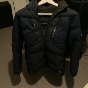 Sailracing jacka - Mörkblå Sailracing puffer jacka.  Storlek 160 Litet hål på ryggen som går att sy ihop.