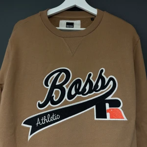 Jättefin sweatshirt från Hugo Boss - Säljer en snygg brun sweatshirt från HugoBoss med ett stort tryck på framsidan där det står 'Boss Athletic'. Tröjan är aldrig använd, bara hängt i min garderob. Storlek M. 