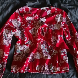 Röd blommig blus - Säljer en superfin röd blus med blommigt mönster från H&M, knappast använd. Den har långa ärmar och en söt knytning framtill. Perfekt för både vardag och fest! 🌸