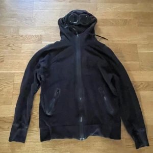 CP Company Hoodie - Storlek: S Köpt på Miinto.se Säljes på grund av att den inte passar längre Kostar ungefär 3300:- på cpcompany.com Väldigt sparsamt använd och tvättad fåtal gånger