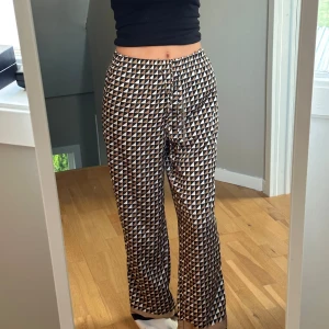 Mönstrade byxor med geometriskt mönster - Säljer ett par snygga byxor med ett coolt geometriskt mönster i svart, vitt och beige. De är högmidjade och har en loose passform som ger en avslappnad stil. Perfekta för både vardag och fest!