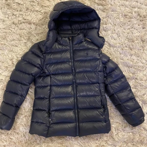 Polo Ralph Lauren dunjacka - I storlek 12-14 år. I överlag mycket bra skick. Fel på dragskedjan på vänstra fickan där den inte går att stänga. Nypris runt 3000 kr.