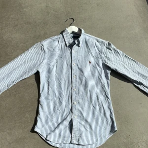 Ralph Lauren skjorta - Säljer en snygg och stilren randig skjorta från Ralph Lauren i storlek S. Skjortan är slim fit och har ett klassiskt blått och vitt randigt mönster. Den är långärmad och har en broderad logga på bröstet. Perfekt för både vardag och fest!