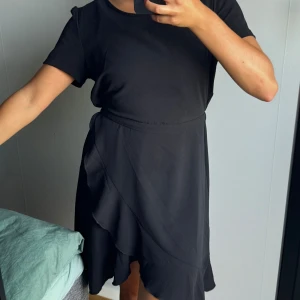 Klänning med volang  - Svart klänning med en slitsvolang och resår i midjan. 