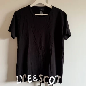 Svart t-shirt från Lyle & Scott - Snygg svart pyjamas t-shirt från Lyle & Scott med stort vitt tryck längst ner. Texten har blivit lite skrynklig men annars bra skick. Storlek s