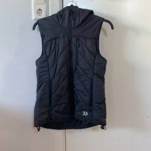 Svart quiltad väst från 157 - Snygg svart quiltad väst från 157 i storlek XS. Västen har en dragkedja framtill och en praktisk huva. Perfekt för lager-på-lager under kyligare dagar.
