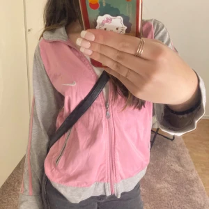 Rosa och grå jacka från Nike - Säljer en sportig rosa och grå jacka från Nike med dragkedja framtill. Jackan har långa ärmar och två fickor. Perfekt för en avslappnad stil eller träning. 🩷